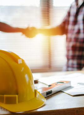 yellow safety helmet on workplace desk with construction worker team hands shaking greeting start up plan new project contract in office center at construction site, partnership and contractor concept