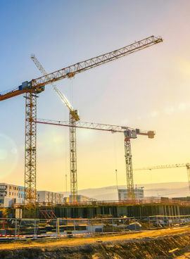 Large construction site including several cranes, with clear sky and the sun