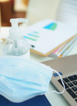 medical mask and hand disinfectant on table in home office