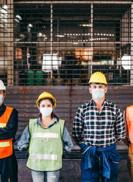 Group of industrial or engineer corporate workers wear protective mask and hard hat helmet standing line up in front of factory lock down prevention for Coronavirus or COVID-19 epidemic outbreak