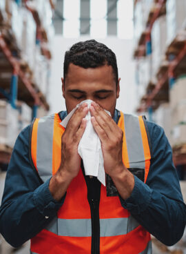 Young sick african warehouse worker blowing nose while working wearing safety vest