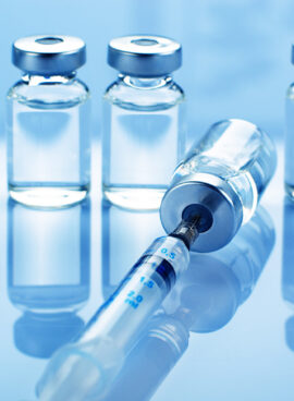 Vial with liquid drug as vaccine dose flu shot along with syringe for injection treatment on medical table. Vaccination or immunization care concept background.