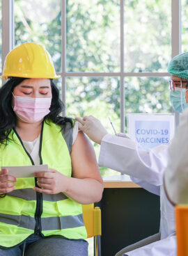 Worker man sitting to getting covid vaccine, with nurse injecting vaccine to get immunity for protect virus. Vaccination for Essential Workers in clinic healthcare at industrial factory.