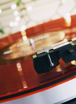 Red vinyl record closeup on a dark background. A ray of light on a piece of vinyl. Sound technology for DJ to mix and play music. Stylus with needle. Christmas lights bokeh reflected on label surface