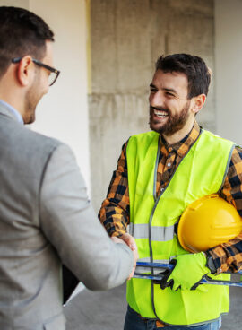 Smiling construction worker shaking hands with supervisor while standing in building in construction process.