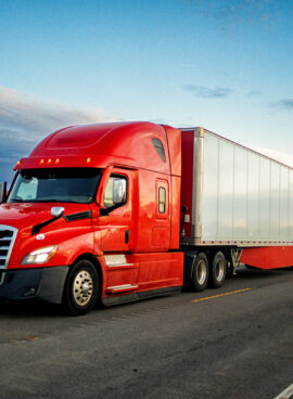 Brightly Red Colored Semi-Truck Speeding on a Two-Lane Highway with Cars in Background Under a Stunning Sunset in the American Southwest