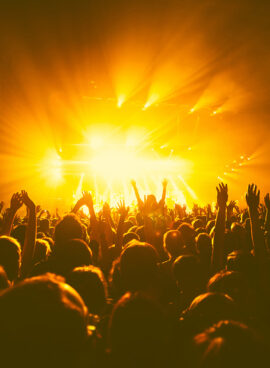 A crowded concert hall with scene stage orange and yellow lights, rock show performance, with people silhouette, colourful confetti explosion fired on dance floor air during a concert festival